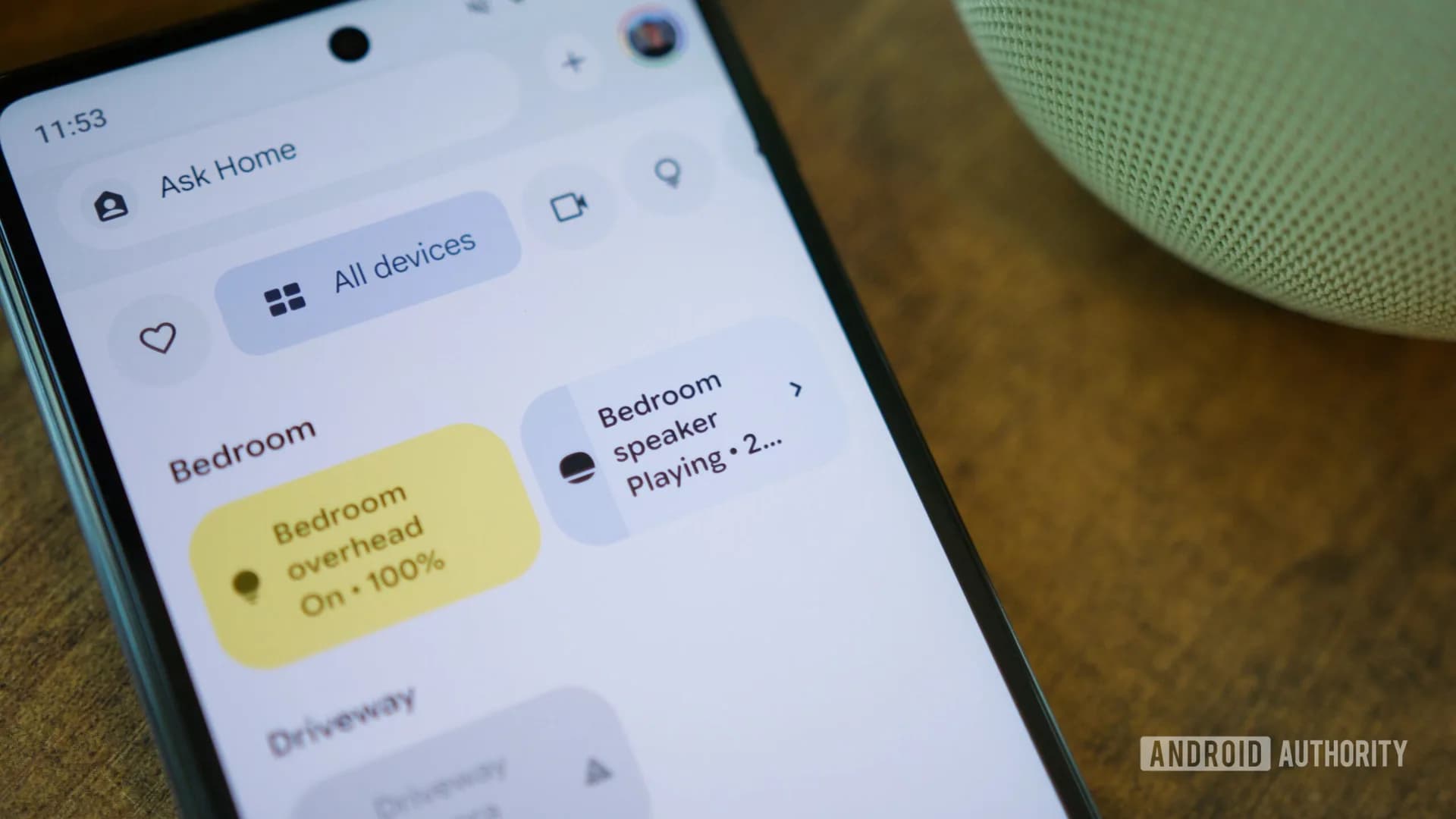 A smart display showing Google Home controls next to an illuminated smart bulb on a wooden side table.