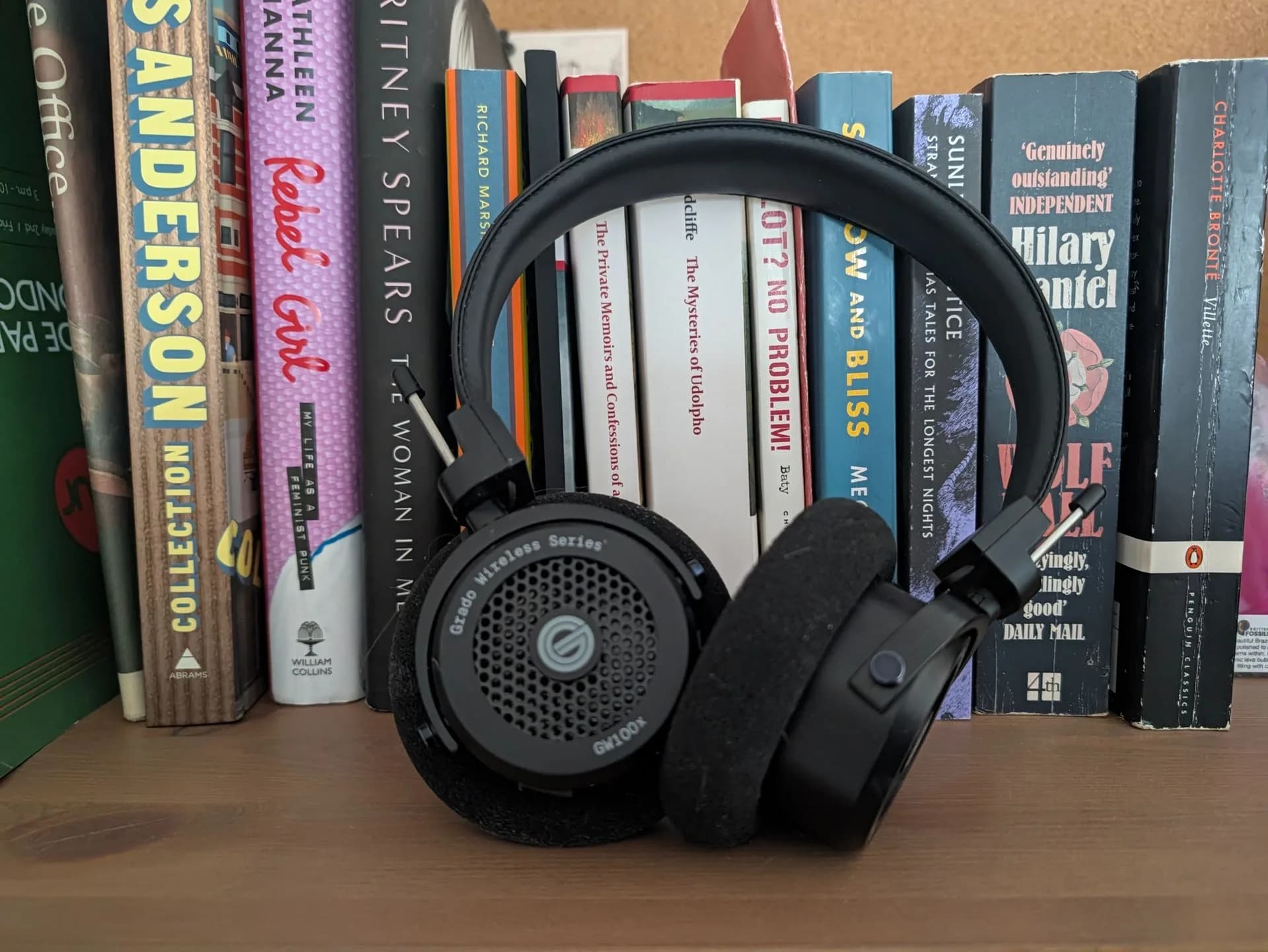 A pair of open-back wireless headphones resting on a wooden surface next to a smartphone.