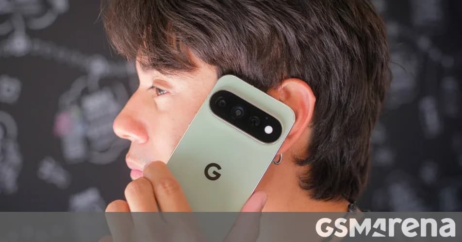 Google Pixel 11 Pro in Obsidian resting face up on a plain grey surface beside a charging cable.