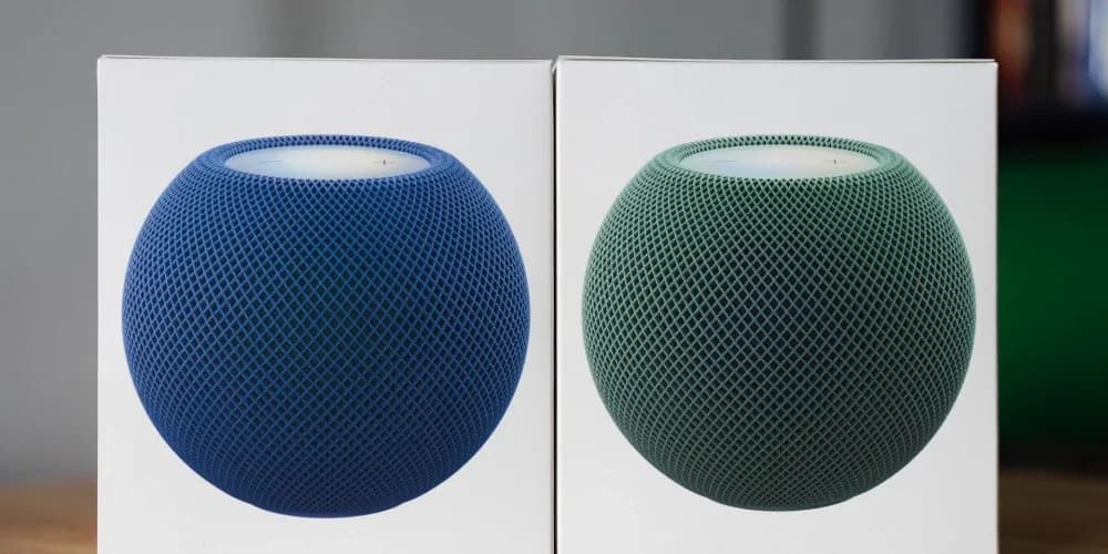 Apple HomePod mini 2 smart speakers in green and blue woven fabric colorways on a wooden surface