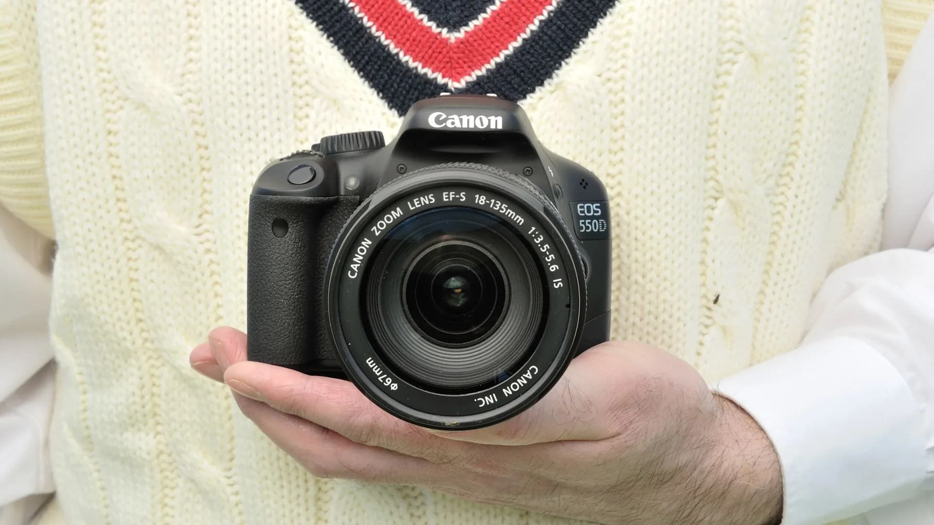 Canon EOS 550D DSLR with 18-55mm kit lens, held in hand against blurred background