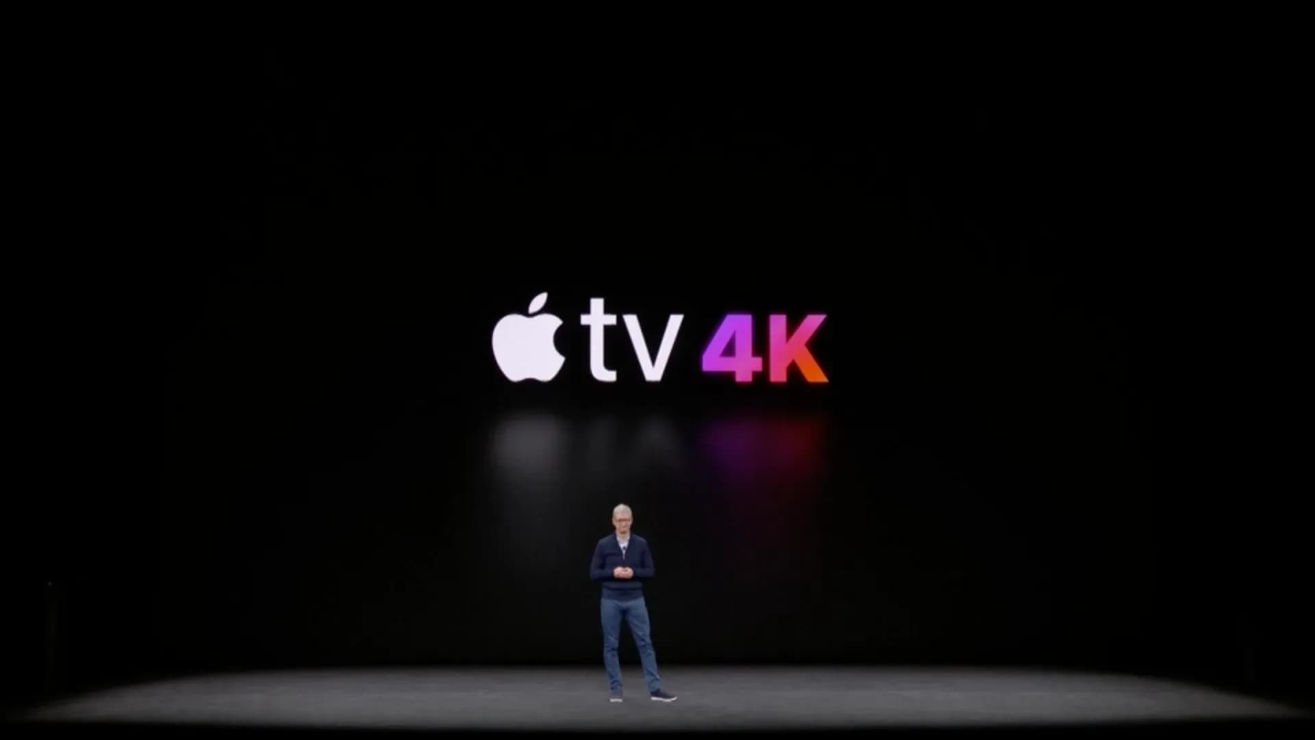 An Apple TV 4K set-top box sitting beside a Siri Remote on a wooden table.