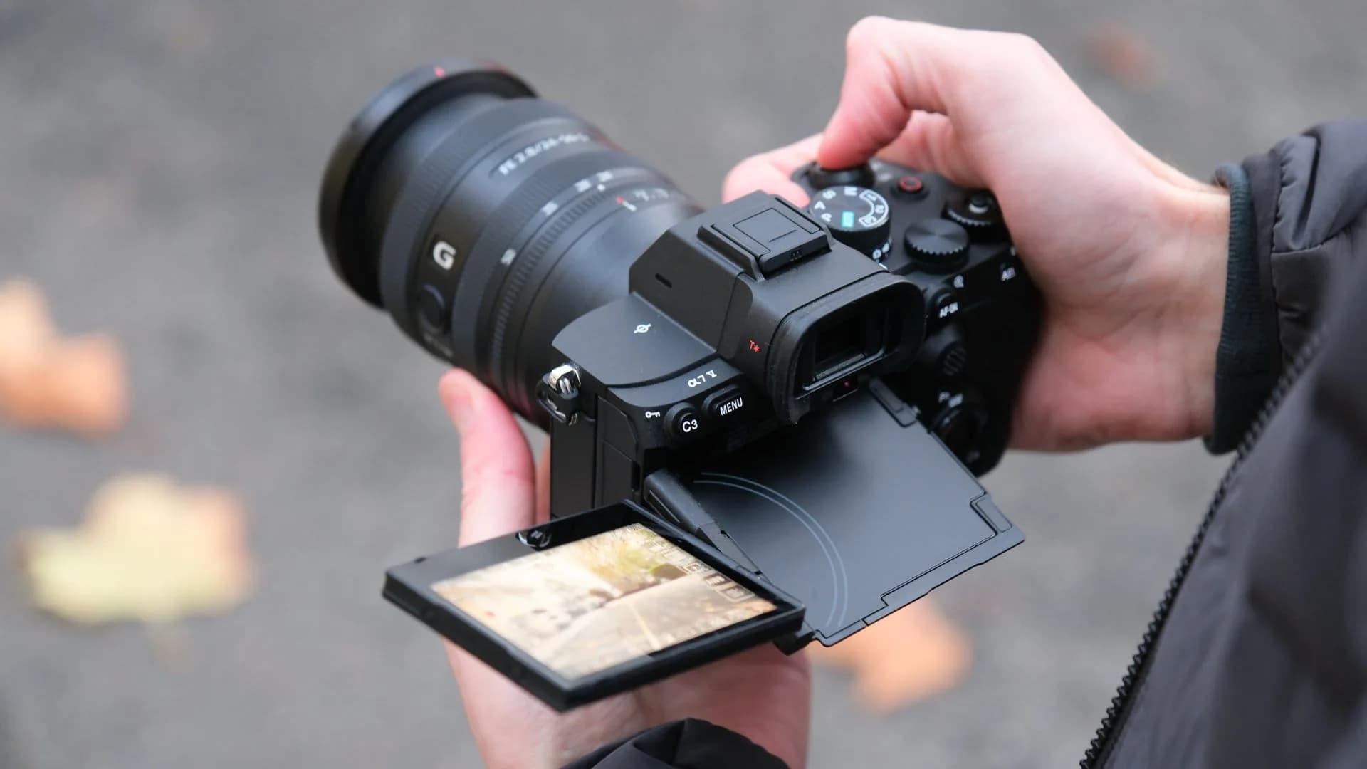 A black Sony A7 V mirrorless camera fitted with a zoom lens on a neutral surface.
