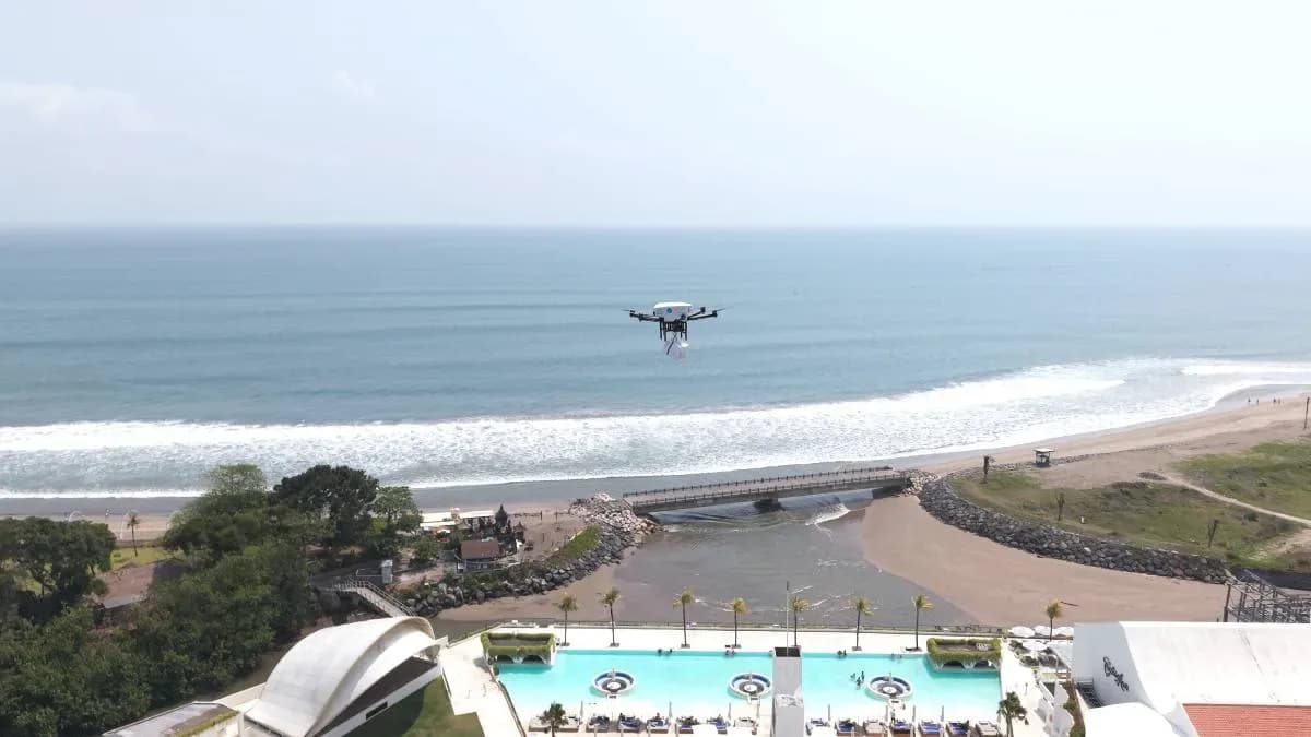 A delivery drone carrying a cargo compartment flies over a coastal landscape.