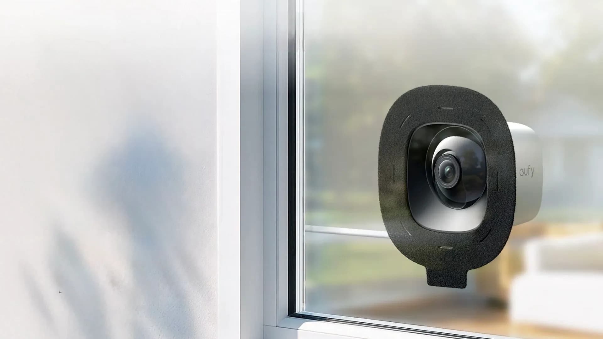 Eufy E10 Window Camera mounted directly against the inside of a glass window looking out at a driveway