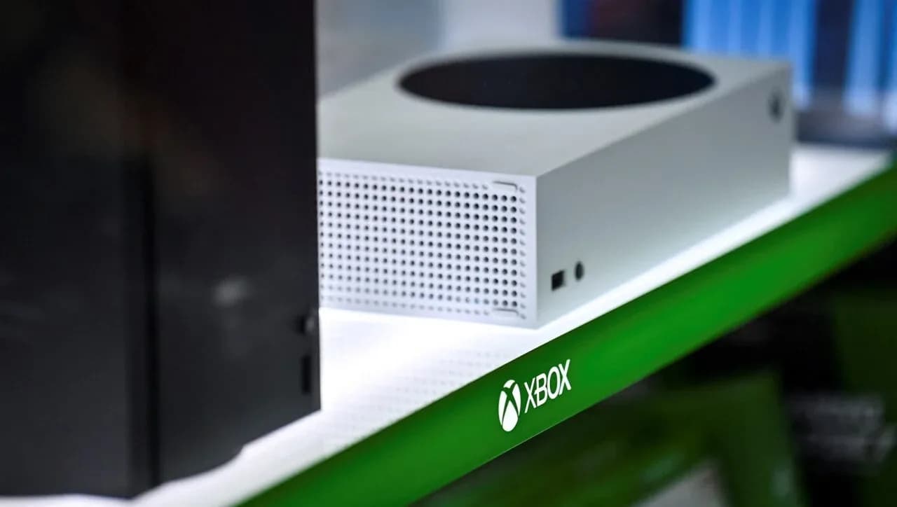 An Xbox Series X console sits on a shelf next to a controller.