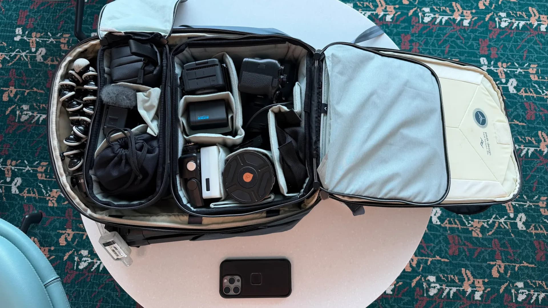 A camera bag open on a table showing a GoPro Mission 1 Pro ILS camera body alongside two compact manual-focus lenses and other travel gear.
