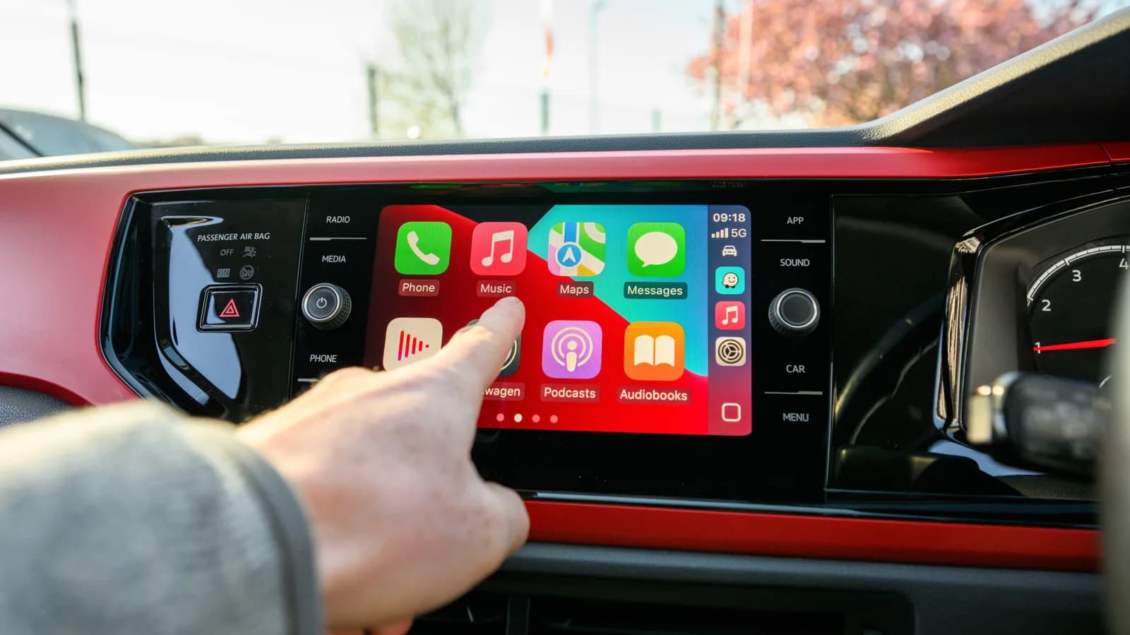 A car dashboard screen running Apple CarPlay with app icons for navigation and audio apps visible