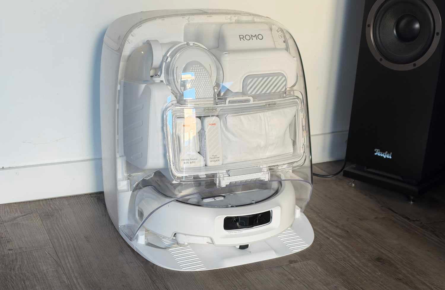 DJI Romo 2 robot vacuum and transparent docking station standing on a hard floor.