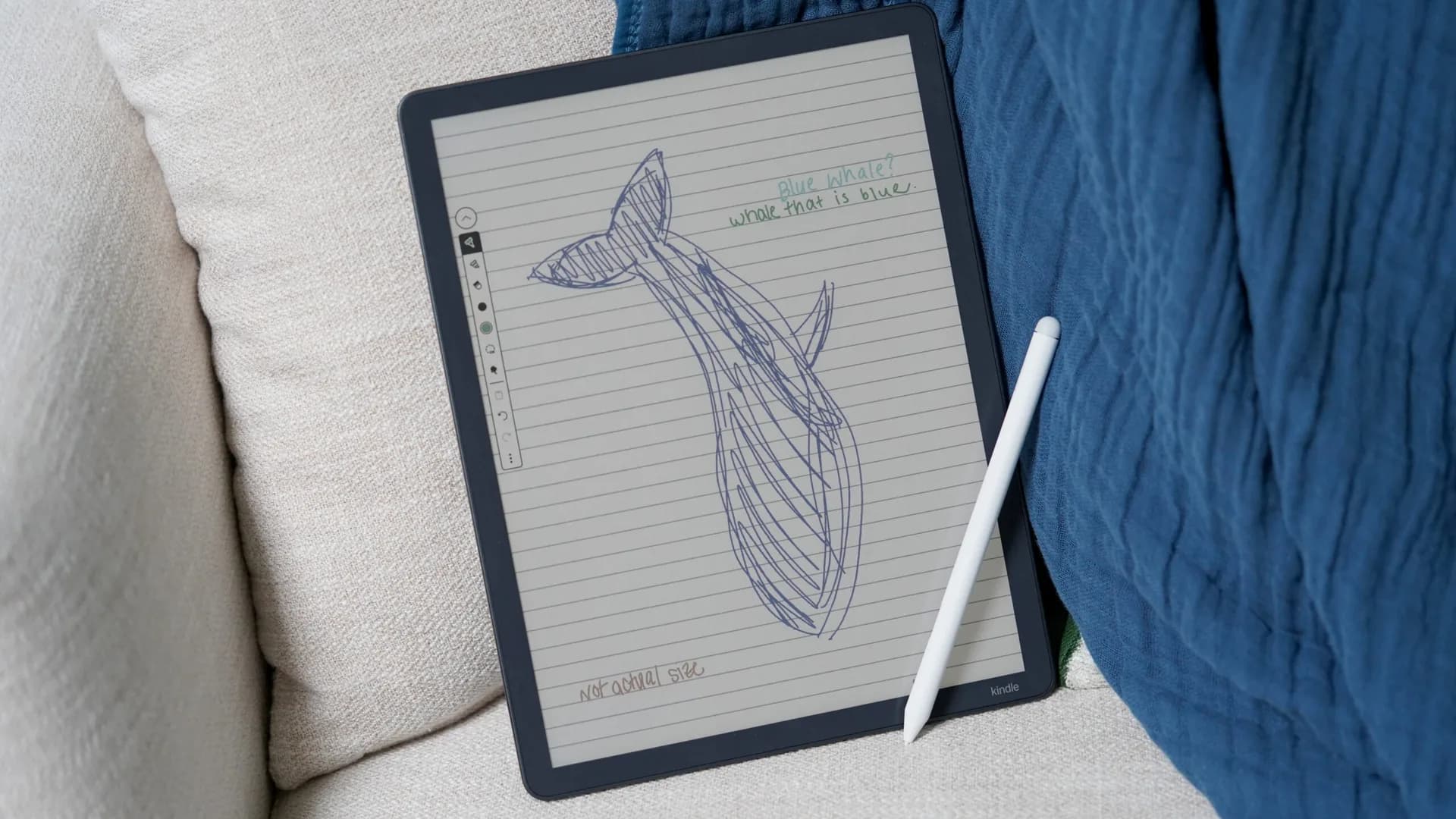 Amazon Kindle Scribe displayed on a desk with its accompanying stylus resting beside the screen.