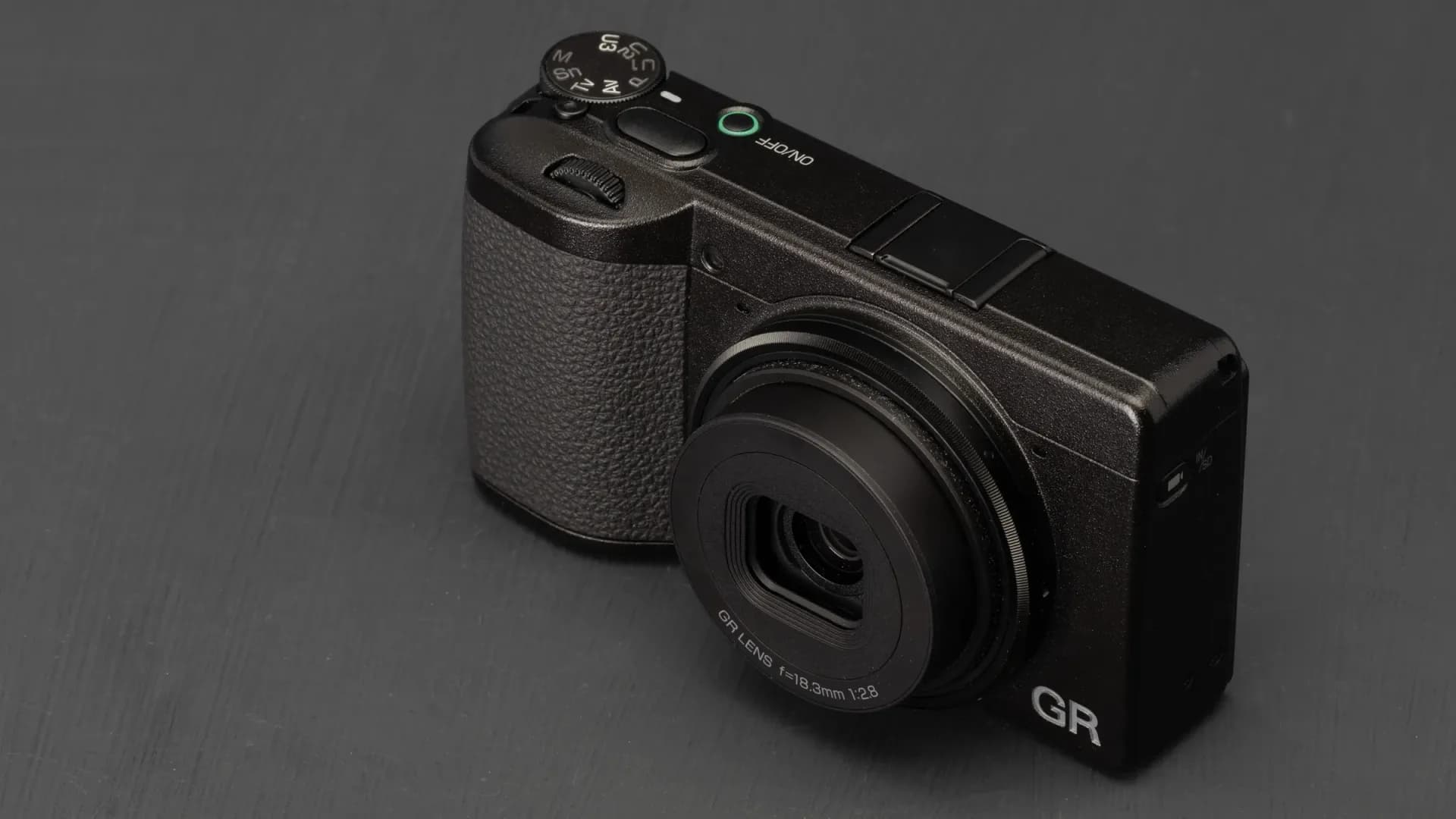 Ricoh GR IV camera resting on a concrete ledge, front view, showing its minimalist silver body and fixed lens