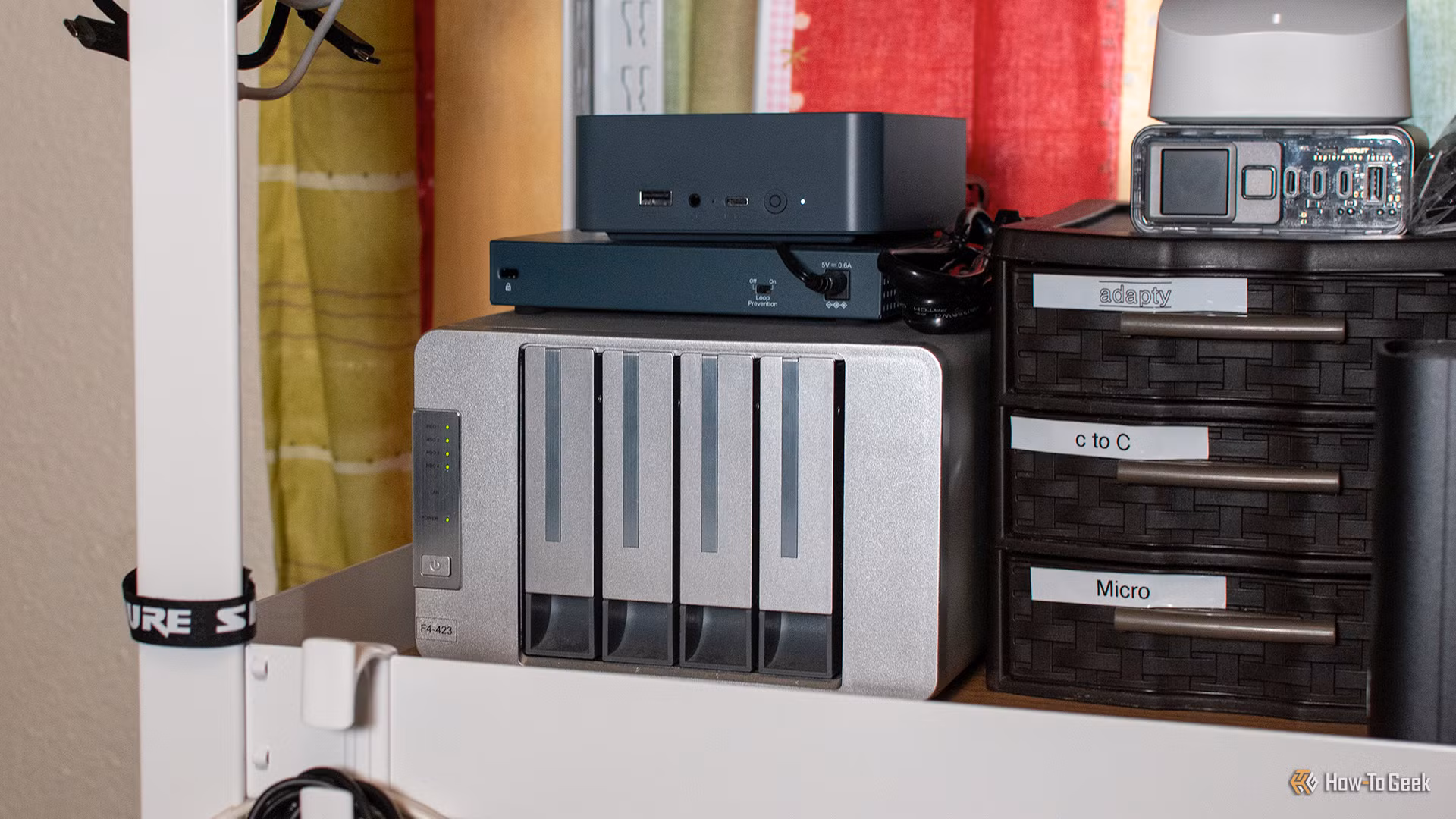 A compact mini PC sitting flat on a wooden desk beside an external storage drive.