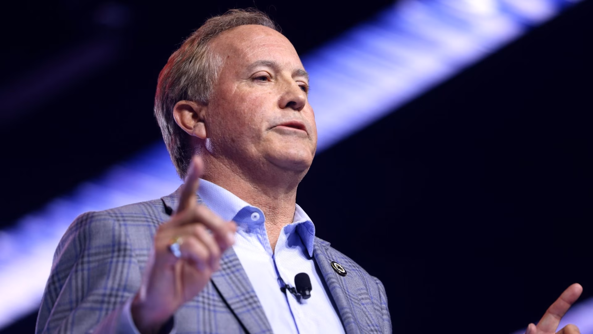 Texas Attorney General Ken Paxton speaking at a podium at AmericaFest 2025 in Phoenix