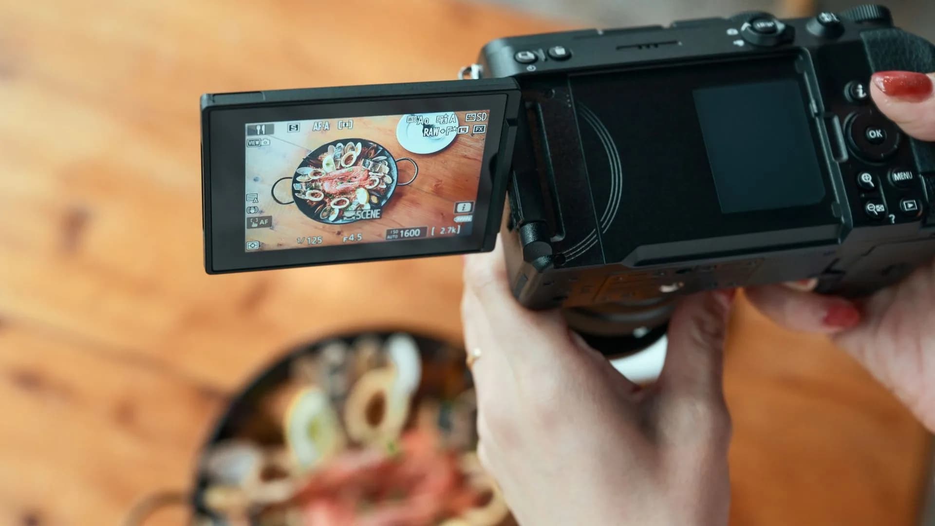 A photographer holding a mirrorless camera with the rear LCD screen tilted upward during an outdoor photo shoot.