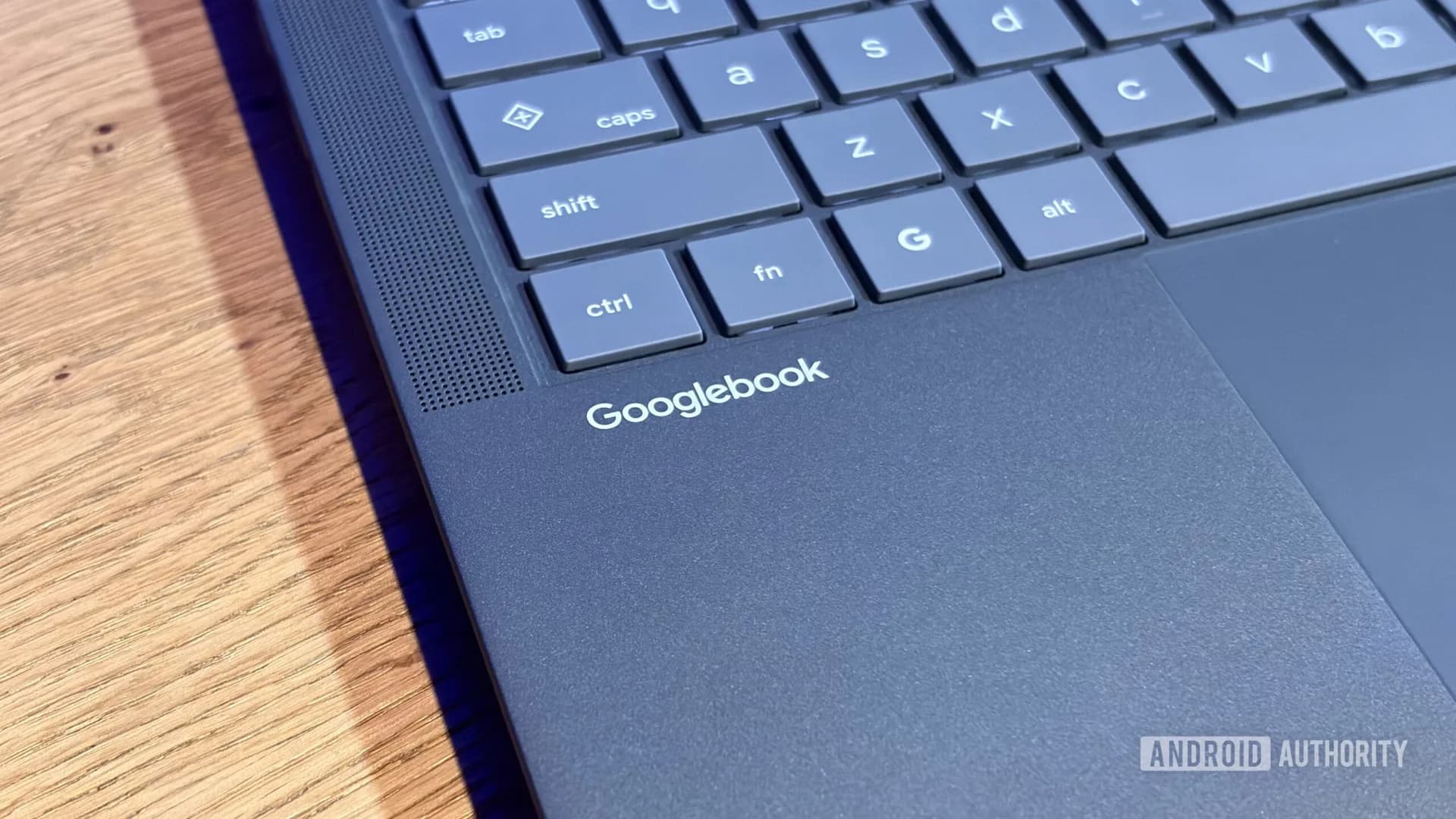 A Googlebook laptop open on a wooden desk showing app icons