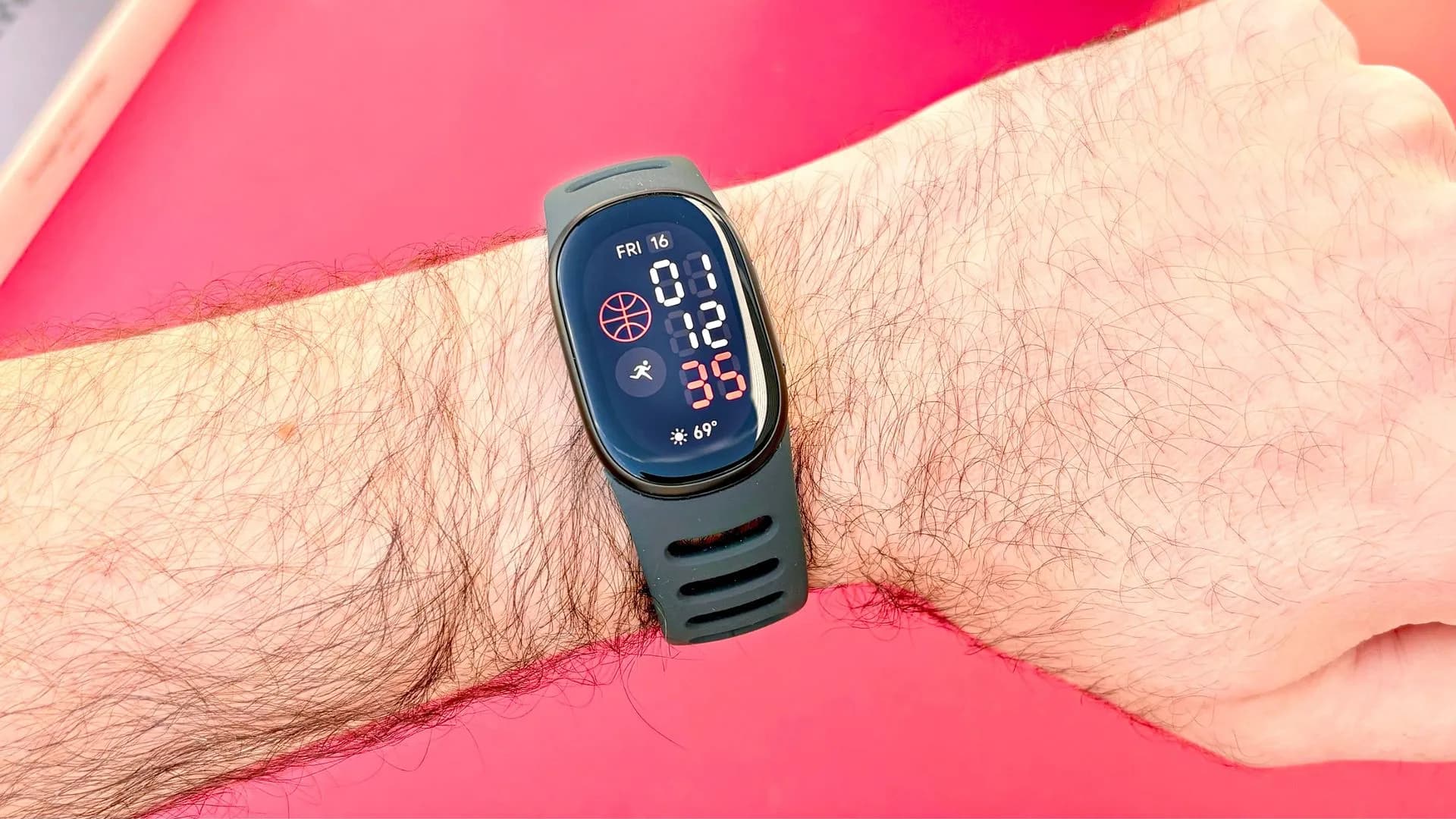 A Fitbit Edge fitness tracker with an AMOLED display worn on a wrist, shown next to its charging accessories.
