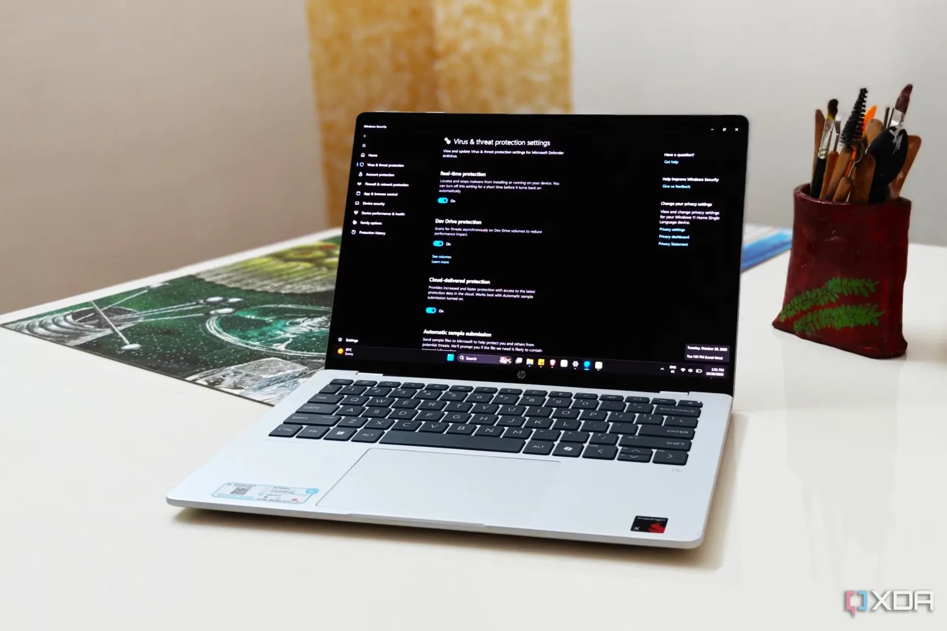 A slim Windows 11 laptop open on a wooden table displaying the Windows Security settings menu.