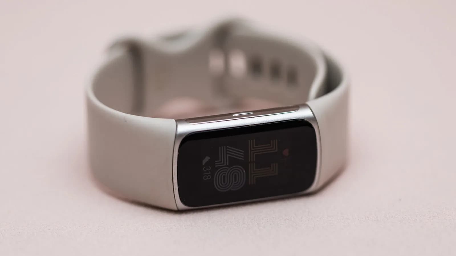 Close-up of a teaser image for Google's Fitbit Edge fitness tracker showing a metal chassis and side button against a Canyon-colored background.