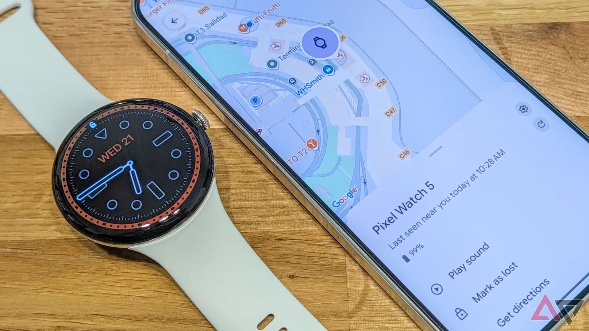 A Pixel Watch 5 shown on a wrist near an airport security tray with a smartphone displaying the Find Hub app.