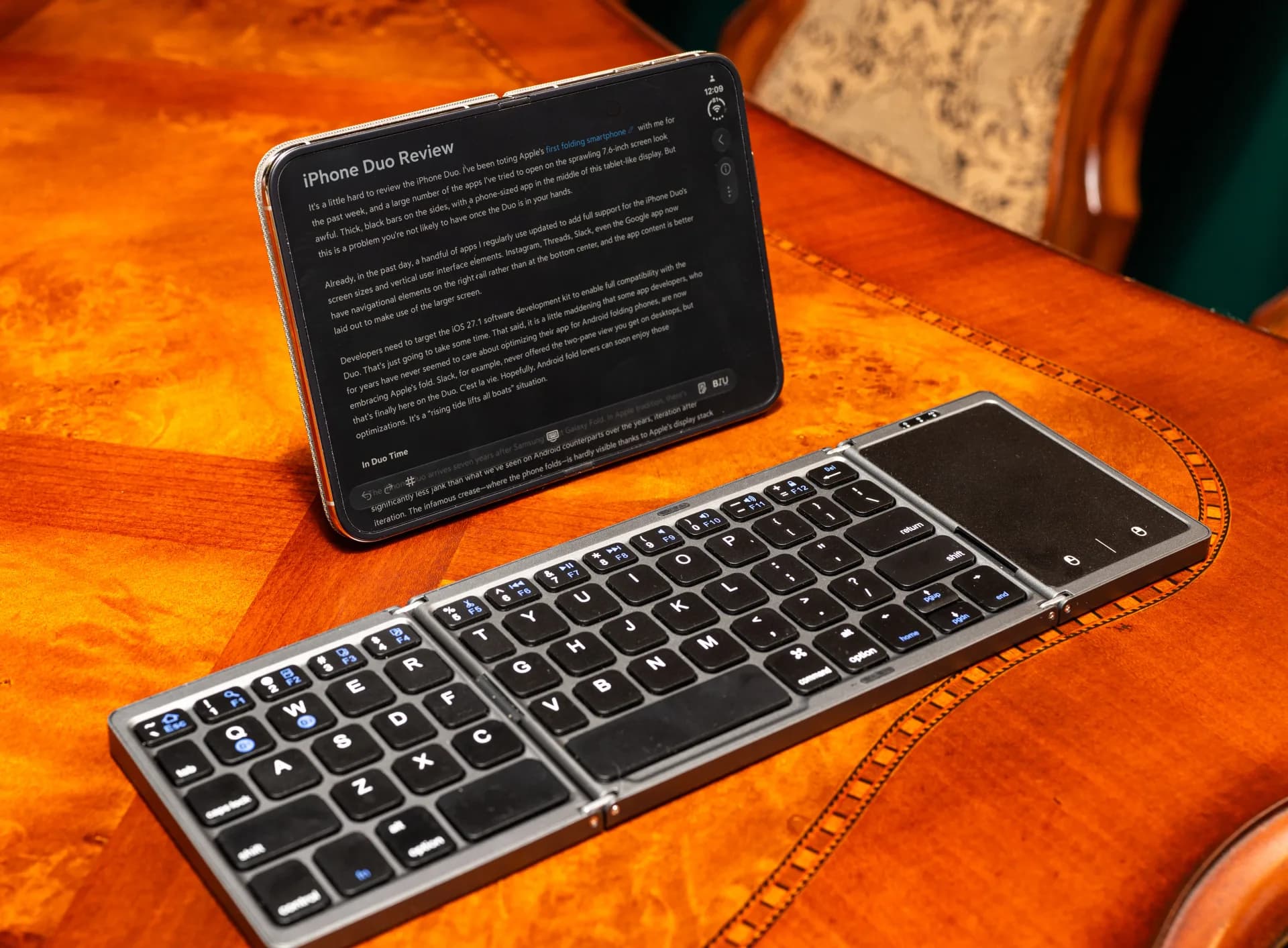 Apple's iPhone Duo folding smartphone shown open with its 7.6-inch inner display, propped on a kickstand case next to a compact keyboard.