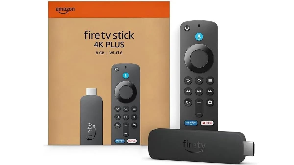 Amazon Fire TV Stick streaming device resting beside its voice remote controller on a dark surface.