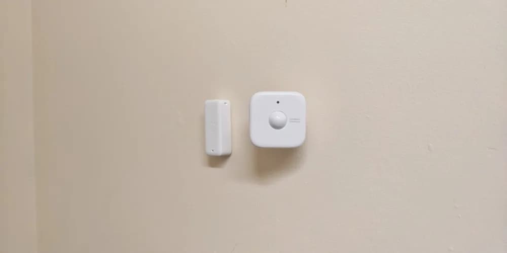 An IKEA KLIPPBOK water leak sensor placed next to a sink, with a smartphone showing a Homey Pro notification reading 'Leak detected — Kitchen sink'.
