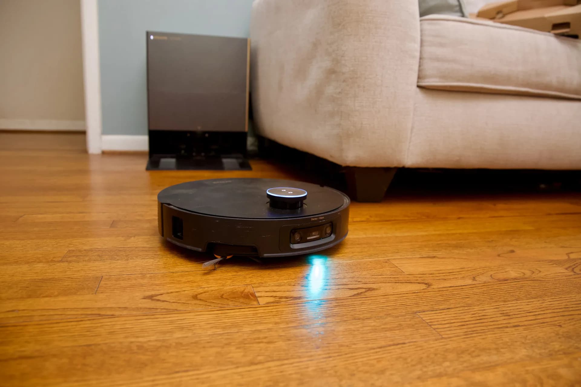 Robot vacuum and mop cleaning hardwood floor next to furniture base